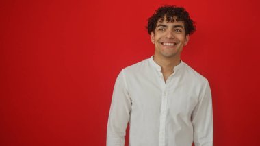 Beyaz tişörtlü gülümseyen genç bir İspanyol, izole edilmiş kırmızı arka planda duruyor.