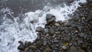 Kaya kıyısı ve okyanus dalgaları Lanzarote 'un siyah taşlarına çarpıyor. Gün ışığında kanarya adaları doğal kıyı manzarasını sergiliyor..