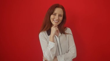 Gülümseyen, kendine güvenen, kızıl saçlı bir kadın izole edilmiş kırmızı bir arkaplanda poz veriyor, çekici ve pozitif..