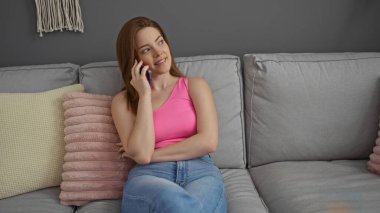 Oturma odasında kanepede oturan genç bir kadın telefonla konuşuyor.