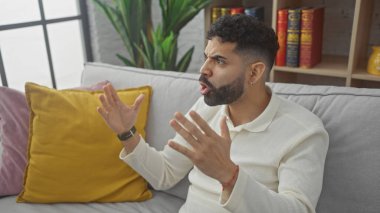 Sakallı genç İspanyol adam evde bir kanepede otururken hayal kırıklığına uğramış görünüyor..