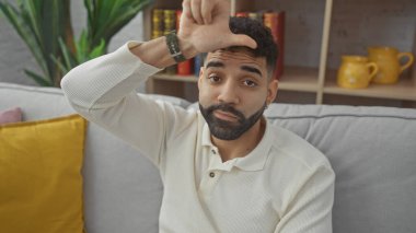 Sakallı, düşünceli bir Latin adam rahat bir oturma odasında oturur ve tefekkür eder..