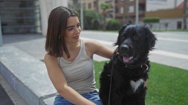 Genç ve güzel bir İspanyol kadın şehir parkında evcil labrador köpeğiyle güneşli bir günün tadını çıkarıyor..