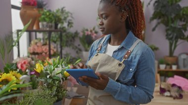 Genç Afrikalı Amerikalı kadın bitkilerle dolu renkli bir çiçekçide tablet kullanıyor..