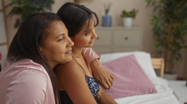 Anne ve kızı sıcak bir yatak odası ortamında birlikte oturup sıcak bir atmosferle aile sevgisini ve yakınlığını gösteriyorlar.