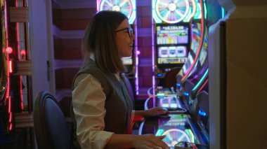 Las Vegas Kumarhanesi 'nde kumar oynayan bir kadın. Parlayan kumar makinelerinin yanında gülümsüyor..