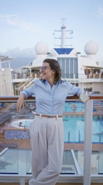 Gemi güvertesinde, tropik bir içecekle gülümseyen, okyanus manzarası ve güneş ışığının tadını çıkaran, lüks bir çevrede tatil rahatlığını somutlaştıran bir kadın.