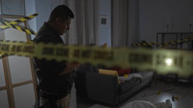 Odaklanmış İspanyol bir adam, loş ışıklandırılmış bir suç mahallini sarı bir polis bandıyla inceliyor..