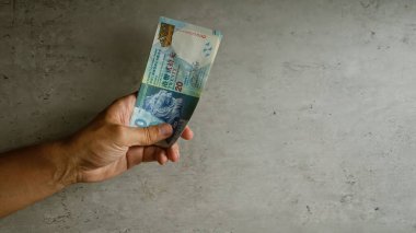 Elele tutuşan Hong Kong dolarları görünür parmaklarıyla beton zemine karşı banknotları kavrıyor, belirgin para birimi özellikleri sergiliyor..
