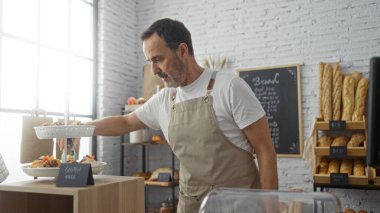 Ekmek ve hamur işleri sergilenen bir fırında çalışan İspanyol kıdemli bir adam, parlak, modern bir iç mekanda glütensiz bir tabela kuruyor..