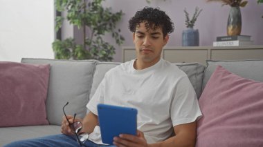 İspanyol adam elinde tabletle evde uzanıyor, rahat koltukta gözlük takıyor, içerisi sakin..