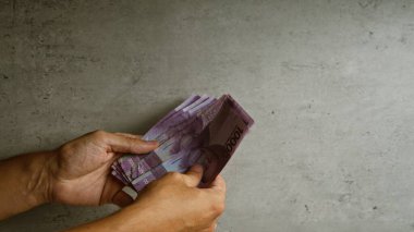 Elleri somut bir arka planda Endonezya rupia banknotlarını sayıyor