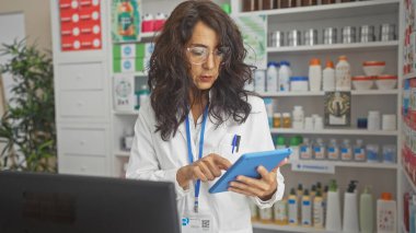 İyi stoklanmış bir eczanenin içindeki tabletteki ilaç bilgilerini inceleyen orta yaşlı kadın eczacı..