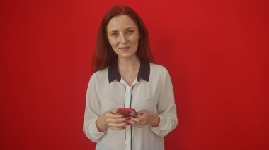 Kızıl saçlı, kendine güvenen genç bir kadın, telefonuyla kırmızı duvara mesaj atıyor.