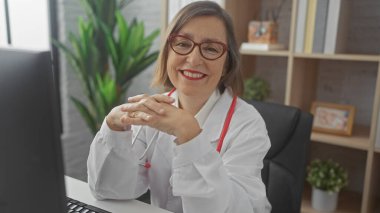 Klinikte bitkiler ve bilgisayarla poz veren beyaz önlüklü gülümseyen kadın profesyonellik ve samimiyet yayıyor..