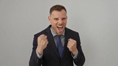 Heyecanlı bir iş adamı, beyaz bir arkaplan karşısında yumruklarını sıkar. Kurumsal ortamda başarı ve coşku yayar..