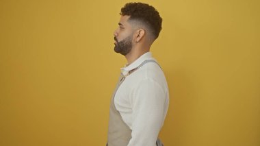 Sakallı şık bir İspanyol genç adam, izole edilmiş sarı bir arka plana karşı, modern erkekliği tasvir ediyor..