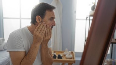 Sakin atmosferi ve yumuşak ışıklandırması olan kaplıca odasında yüzü incelenen bir adam, kapalı bir salon ortamında olgun güzellik ve sağIık odağı sergiliyor..