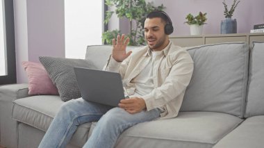 Modern bir oturma odasında, bilgisayar kullanan ve kulaklık takan genç bir İspanyol..