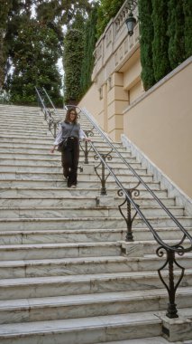 Monaco 'da mermer merdivenlerden inen bir kadın lüks bir ortamda zarafet ve gençlik saçıyor. Manzaralı mimari ve yemyeşil manzarayla ön plana çıkıyor..