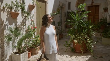 Genç İspanyol kadın locorotondo, puglia, İtalya 'nın büyüleyici eski sokaklarında güneşli bir günün tadını çıkarıyor. Etrafı yemyeşil bitkilerle ve şehir merkezindeki beyaz tarihi binalarla çevrili..