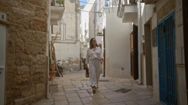 Polignano 'da büyüleyici dar sokaklarda yürüyen İspanyol bir kadın kısrak, puglia, İtalya, günlük kıyafetler giymiş ve bir çanta tutuyor..