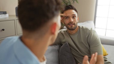 İki eşcinsel erkek, rahat bir oturma odasında, rahat ve samimi bir anı paylaşarak vakit geçiriyorlar..