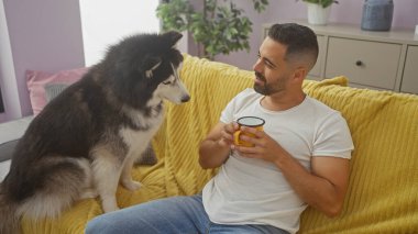İspanyol bir adam ve Husky sarı bir kanepede rahat bir oturma odasında, kahve içerken biraz zaman geçiriyorlar.