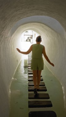 Lagomar, Lanzarote, Kanarya Adaları 'nda sanatsal bir tünelde yürüyen genç bir kadın, arka planı aydınlatan güneş ışığı ile basamak taşları üzerinde dengede duruyor.