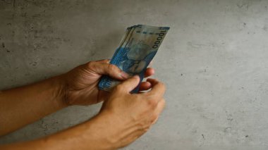 Şili pesolarını iki eliyle beton duvar arkasında sayan bir adam.