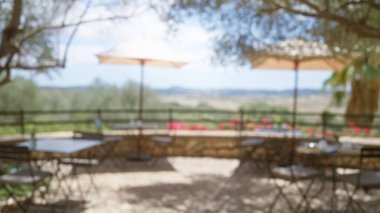 Mallorca 'daki bulanık kafeterya sahnesi. Şemsiyelerin altında çözünmüş masalar ve sandalyeler. Manzaralı, güneşli, Akdeniz arka planının ortasında.. 