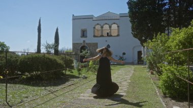 A young hispanic woman twirls outside a beautiful villa in puglia, italy, amidst lush greenery on a sunny day. clipart