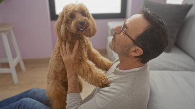 Orta yaşlı İspanyol bir adam sıcak bir oturma odasında kanişiyle kaynaşırken gülümsüyor.