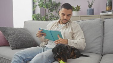 Genç bir İspanyol adam evdeki kanepede yanında köpeğiyle birlikte sükunet ve arkadaşlık tasvir eden bir kitap okuyor..