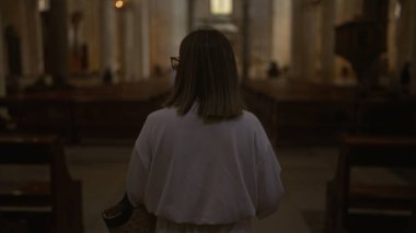 İtalya 'da loş ışıklı bir kilisede oturan genç bir İspanyol kadın. Arka planda ahşap sıralar ve aydınlatmalı vitray pencereler var..