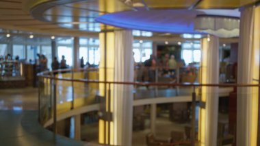 Kapalı bir alanda, arka planda insanların bulunduğu lüks bir yolcu gemisinin zarif iç tasarım detaylarını vurgulayan yumuşak bir bokeh parıltısına karşı görüntüsü..