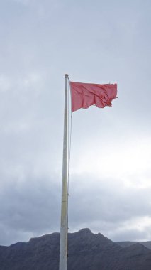 Rüzgarda dalgalanan kırmızı bayrak bulutlu bir gökyüzüne ve gün ışığında dağlık araziye karşı