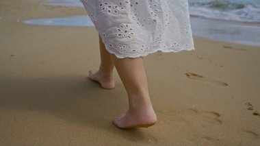 Genç bir İspanyol kadın, pescoluse, puglia, salento, İtalya sahillerinde çıplak ayakla yürüyor. Çiçek desenli beyaz bir elbise giyiyor..