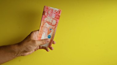 Sarı arka planda Filipinli pezolarla el ele tutuşmak, canlı 50 peso 'luk banknotları gözler önüne seriyor..