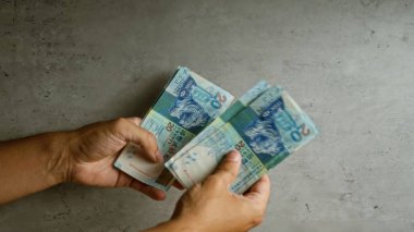 Man holding hong kong dollars against a concrete background, counting money with both hands clearly visible. clipart