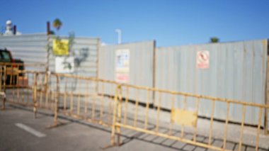 Metal bariyerleri, bulanık arkaplanı ve açık mavi gökyüzü altındaki güvenlik levhası olan inşaat alanının odaklanmamış görüntüsü