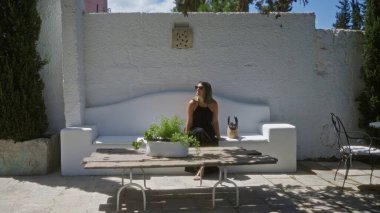 Genç İspanyol kadın Puglia, İtalya 'da bir villada yeşil ve kırsal bir dekoru olan beyaz bir bankta oturuyor, Avrupa' nın güneş ışığının tadını çıkarıyor..