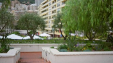 Blurry urban scene in monaco featuring lush greenery and blurred modern architecture under daylight with focus on bokeh effect enhancing an outdoor luxury ambiance. clipart