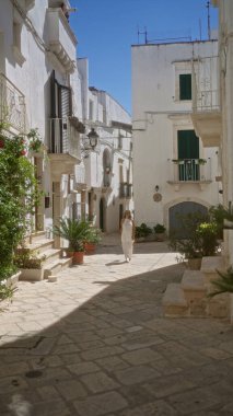 Güzel, genç, İspanyol bir kadın Puglia, İtalya 'da beyaz binalar ve yemyeşil alanlarla çevrili büyüleyici eski kasaba sokaklarında yürüyor..