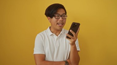Çin 'den gelen genç adam, sarı arka plandaki akıllı telefonuna bakıyor. Gözlüklü ve beyaz gömlekli çekici bir yetişkini gösteriyor.