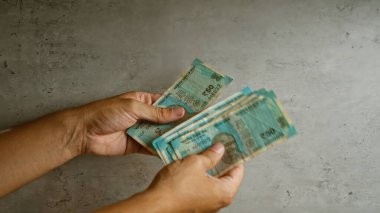 Hindistan 'da finansal işlemleri gösteren, beton bir yüzey üzerinde iki eliyle Hindistan Rupisi sayan bir adam..