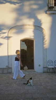 Genç, güzel bir İspanyol kadın Puglia 'da bir İtalyan villasında evin girişinde bir kediyle yürüyor..