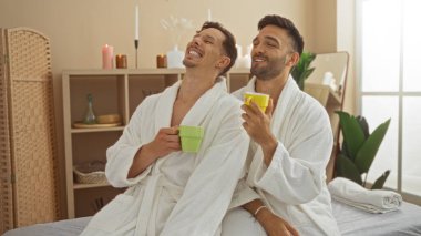 Rahatlatıcı bir spa odasında birlikte vakit geçiren bir çift. Beyaz cüppeli adamlar ellerinde kahve fincanları tutuyorlar. Huzurlu bir sağlık merkezinde sevgi ve rahatlık ifade ediyorlar..