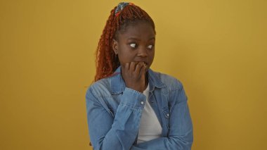 Kot ceketli düşünceli genç siyah bir kadın sarı arka planda poz veriyor..