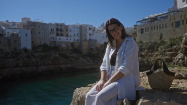 Genç İspanyol kadın polignano manzarasının tadını çıkarıyor. Puglia, İtalya 'da bir kısrak. Sahilde ve denizde arka planda oturuyor..